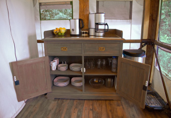 Houten kast met koffiezetapparaten, servies en glaswerk bij SunLodge Safari op Camping Pra'delle Torri, Italië.