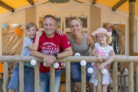 Una familia feliz posando en la terraza de SunLodge Safari en Camping Pra'delle Torri en Italia.