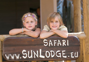 Twee kinderen leunen op een houten bord bij SunLodge Safari op Camping Pra'delle Torri in Italië.