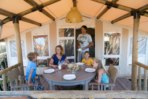 Familia disfrutando de una comida frente a su tienda en SunLodge Safari, Camping Pra'delle Torri, Italia.