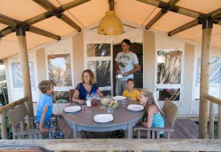 Familia disfrutando de una comida frente a su tienda en SunLodge Safari, Camping Pra'delle Torri, Italia.