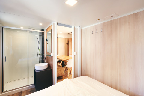 Dormitorio moderno con baño privado y comedor en SunLodge Sabai, con paredes de madera clara.