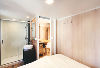 Dormitorio moderno con baño privado y comedor en SunLodge Sabai, con paredes de madera clara.