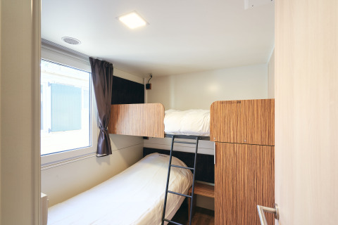 Kamer in SunLodge Sabai met stapelbedden, raam met gordijn en houten kasten in een compacte ruimte.