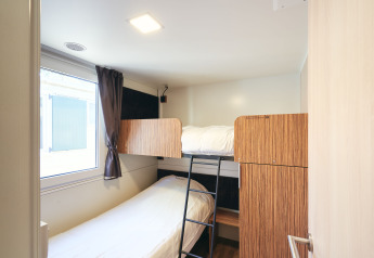 Kamer in SunLodge Sabai met stapelbedden, raam met gordijn en houten kasten in een compacte ruimte.