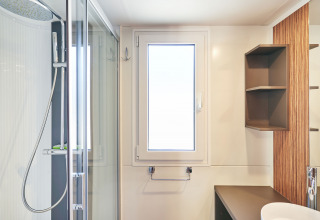 Baño moderno en SunLodge Sabai con cabina de ducha, ventana, lavabo y estantes abiertos en la pared.