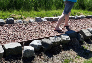 Twee mensen lopen blootsvoets op een grindpad omgeven door stenen bij Camping De Gouwe Stek.