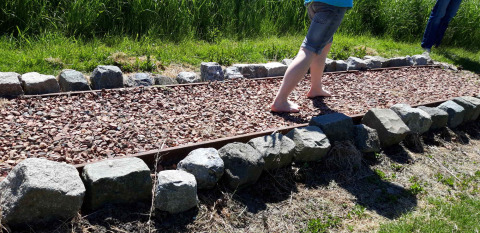 Twee mensen lopen blootsvoets op een grindpad omgeven door stenen bij Camping De Gouwe Stek.
