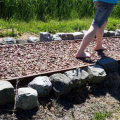 Dos personas caminan descalzas por un sendero de grava rodeado de piedras en Camping De Gouwe Stek, Holanda.