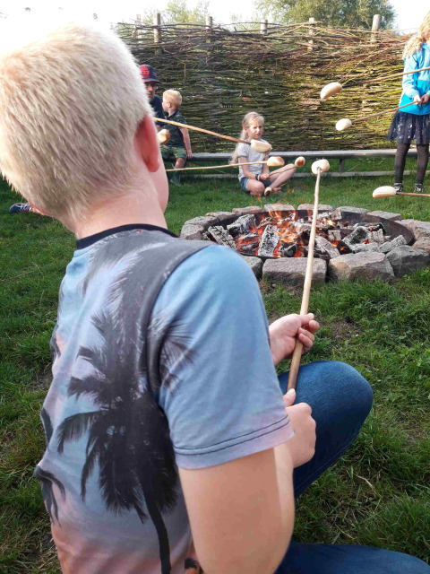 Niños asando pan en palos sobre una fogata en Camping De Gouwe Stek, un parque en Holanda Septentrional.