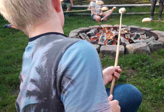 Bambini arrostiscono il pane su bastoncini al fuoco nel Camping De Gouwe Stek, Olanda Settentrionale.