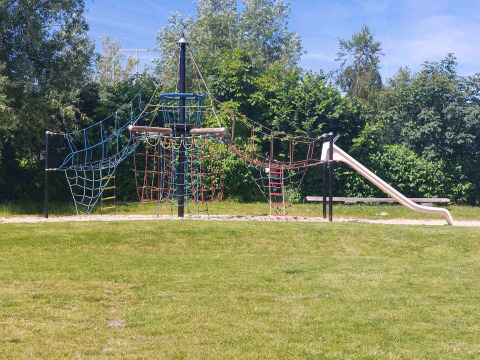 Aire de jeux avec structure d’escalade et toboggan à Camping De Gouwe Stek, entourée de verdure.