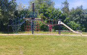 Aire de jeux avec structure d’escalade et toboggan à Camping De Gouwe Stek, entourée de verdure.