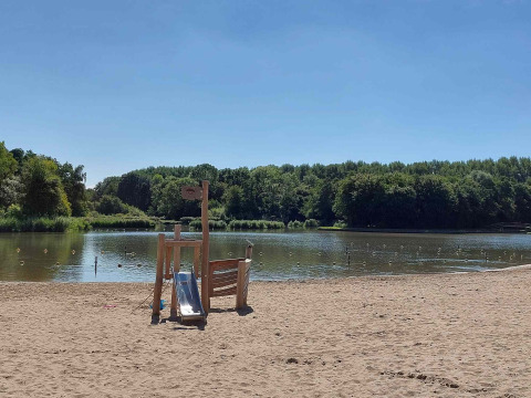 Playa de arena con área de juegos junto al lago y bosque en Camping De Gouwe Stek, Holanda Septentrional.