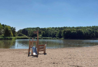 Zandstrand met speeltuig aan een vijver en bos op Camping De Gouwe Stek, Noord-Holland.