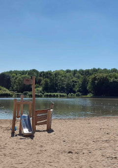 Playa de arena con área de juegos junto al lago y bosque en Camping De Gouwe Stek, Holanda Septentrional.