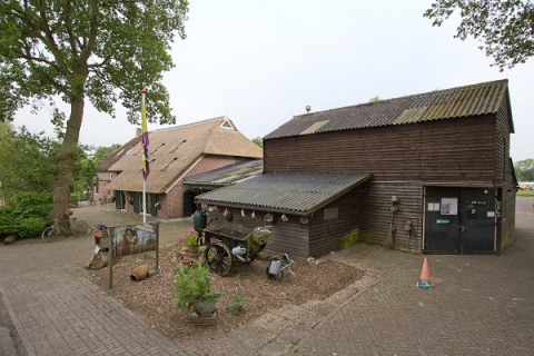 View of Camping de Berghoeve holiday park in Drenthe, Netherlands, showing rustic buildings and a green setting.