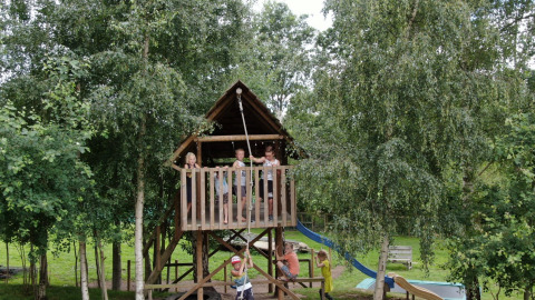 Niños juegan en una casa del árbol con tobogán en un parque vacacional con opciones de glamping.