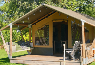 Stoere Safari-Zelt mit überdachter Veranda, Hängesofa und Sitzplätzen inmitten grüner Natur.