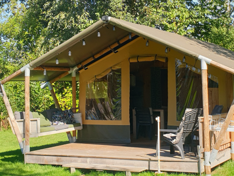 Stoere Safari tent met overdekt terras, zweefbank en buitenzitjes in een groene, natuurlijke omgeving.
