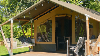 Stoere Safari-Zelt mit überdachter Veranda, Hängesofa und Sitzplätzen inmitten grüner Natur.