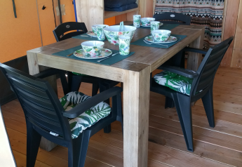 Tavolo da pranzo con quattro sedie nere e stoviglie in una tenda Stoere Safari al Camping de Berghoeve.