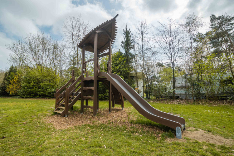 Playground with slide and stairs surrounded by trees at Buitencentrum Hessenheem holiday park, Overijssel.