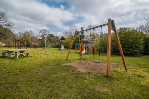 Playground with swings, slide, and a picnic table at Buitencentrum Hessenheem holiday park in Overijssel.