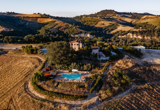 Luftfoto af Agricola La Casetta feriested, omgivet af bakker og marker i Marche-regionen, Italien.