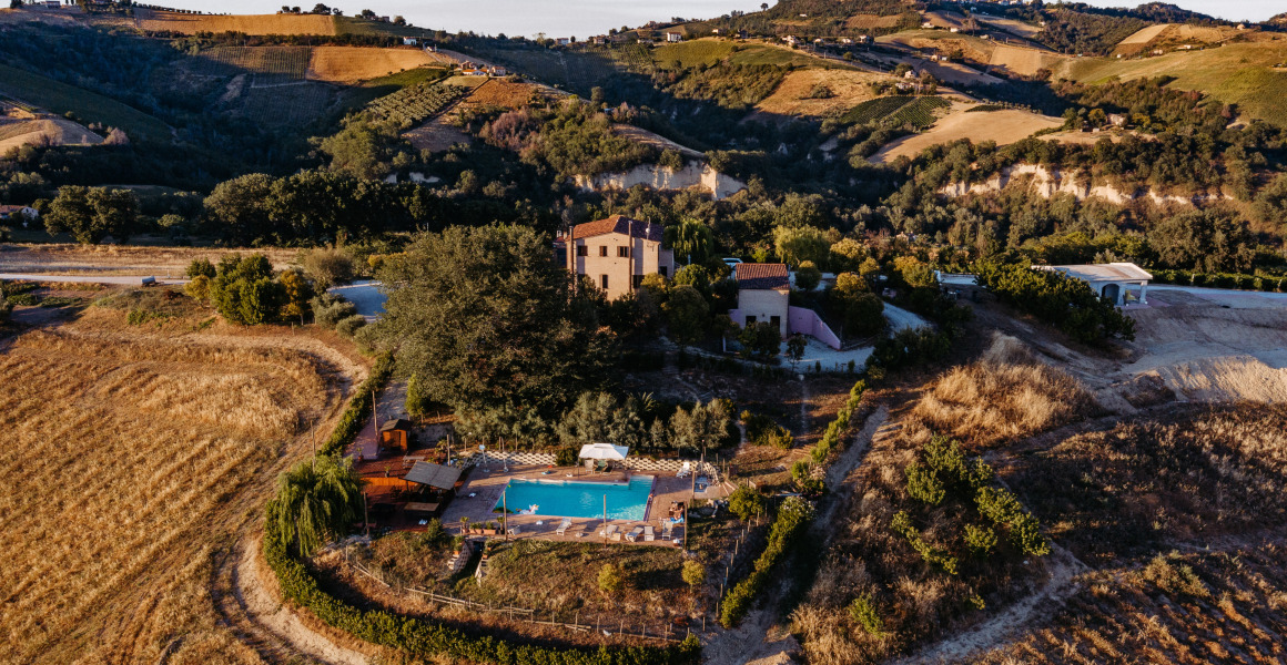 Luchtfoto van vakantiepark Agricola La Casetta, gelegen tussen heuvels en velden in Marche, Italië.