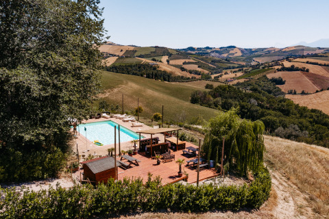 Schwimmbad und Sonnenterrasse von Agricola La Casetta, einem Ferienpark in Marche, Italien, in Hügellandschaft.