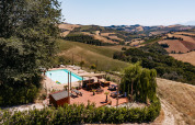 Udsigt over swimmingpool og soldæk på Agricola La Casetta feriepark i Marche, Italien, omgivet af bakker.