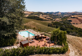 Udsigt over swimmingpool og soldæk på Agricola La Casetta feriepark i Marche, Italien, omgivet af bakker.