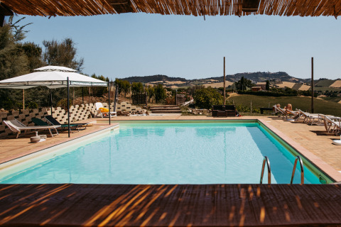 Pool mit Liegestühlen und Sonnenschirm im Ferienpark Agricola La Casetta in Marche mit Hügelblick.