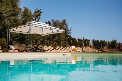 Piscina en Agricola La Casetta, parque vacacional en Marche, Italia, con tumbonas y toldo en un día soleado.