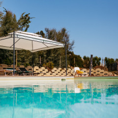 Piscina en Agricola La Casetta, parque vacacional en Marche, Italia, con tumbonas y toldo en un día soleado.