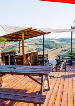 Terraza de madera con bancos y vistas panorámicas a las colinas en Agricola La Casetta, Marche, Italia.