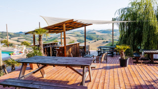 Terraza de madera con bancos y vistas panorámicas a las colinas en Agricola La Casetta, Marche, Italia.