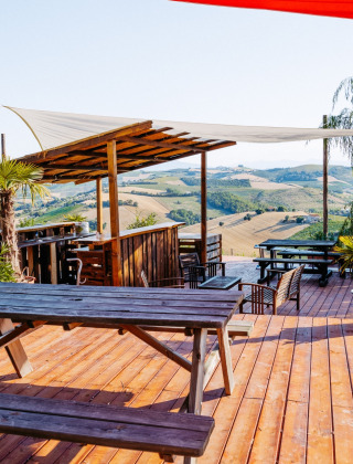 Terraza de madera con bancos y vistas panorámicas a las colinas en Agricola La Casetta, Marche, Italia.