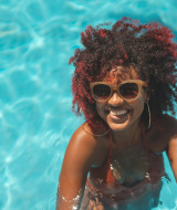 Mujer con gafas de sol sonríe en la piscina de un parque vacacional que ofrece alojamientos glamping.
