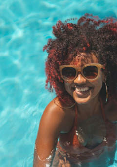 Frau mit Sonnenbrille lacht im Pool eines Ferienparks mit Glamping-Angeboten und genießt den Sommer.