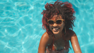 Frau mit Sonnenbrille lacht im Pool eines Ferienparks mit Glamping-Angeboten und genießt den Sommer.