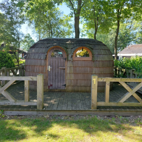 En IGLO Log Cabin ved Camping Emmen i Holland, lavet af træ, omgivet af træer og en træveranda.