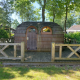 En IGLO Log Cabin ved Camping Emmen i Holland, lavet af træ, omgivet af træer og en træveranda.