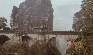 Antiguo puente de piedra sobre formaciones rocosas y naturaleza brumosa cerca de Šluknov, República Checa.