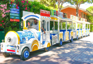 Un colorato trenino Union Lido Shuttle attraversa il villaggio turistico Camping Union Lido Mare in Veneto, Italia.