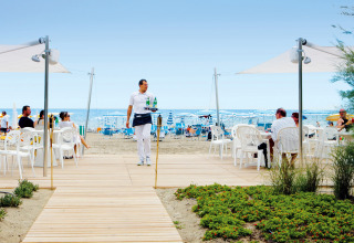 En tjener serverer drikkevarer til mennesker, der slapper af på plaststole ved stranden i Veneto, Italien.