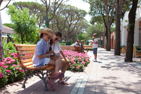 Niños disfrutan sentados en bancos entre flores en el camping Union Lido Mare, parque vacacional en Véneto, Italia.