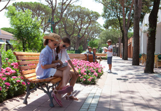 Børn hygger sig på bænk omgivet af blomster og træer i ferieparken Union Lido Mare i Veneto, Italien.