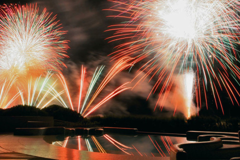 Colorati fuochi d’artificio illuminano la notte sopra Camping Union Lido Mare in Veneto, Italia, visti dalla piscina.
